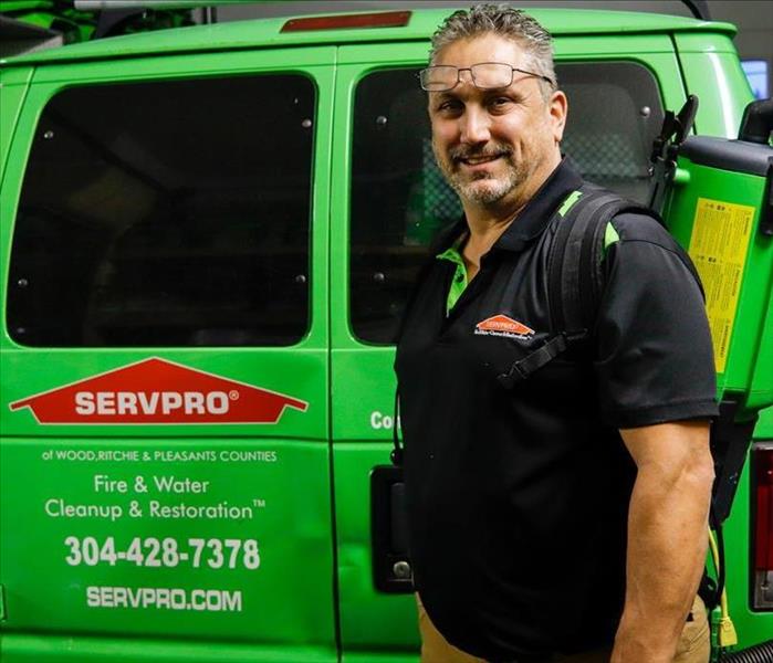 Co-Owner, James Miller, standing and smiling in front of the rear of the SERVPRO van with a vacuum on his back.